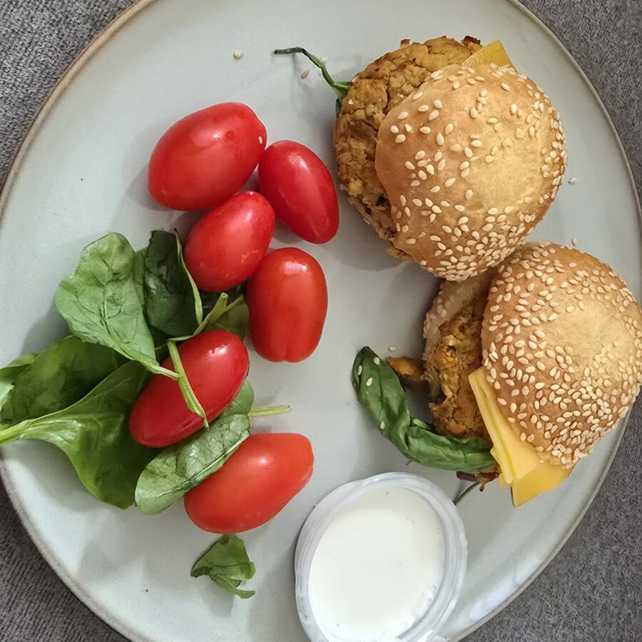 Burger z batata i ciecierzycy z czerwoną cebulą w bułce z sezamem, roszponka z pomidorkami